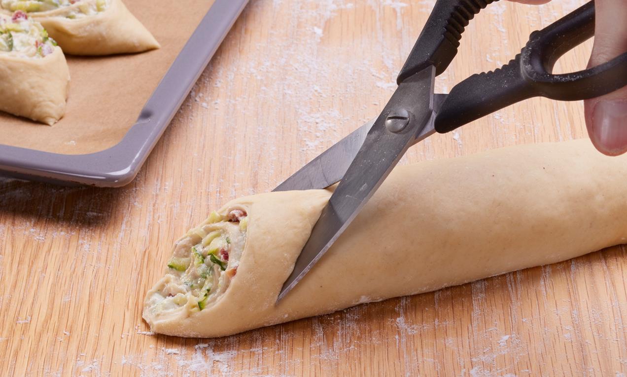 A Pikáns cukkinis virágok süteményt konyhai ollóval vágjuk szeletekre.