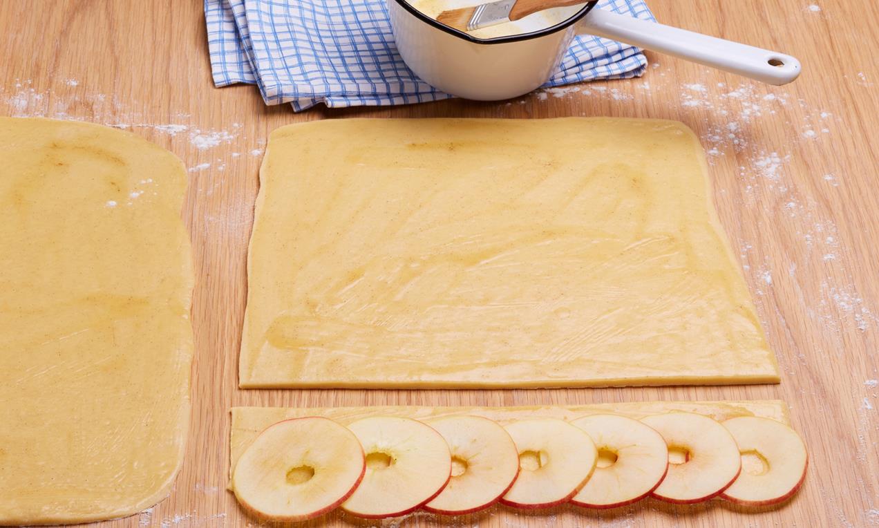 Az almaszeleteket a sütemény kinyújtott tésztaalapjára fektetjük, sorban, átfedéssel.