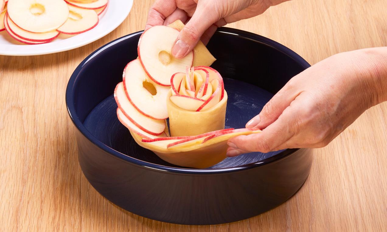 A sütemény almával rétegezett tésztalapjait kerek sütőformában, vagy tortaformában tekerjük egymás köré.