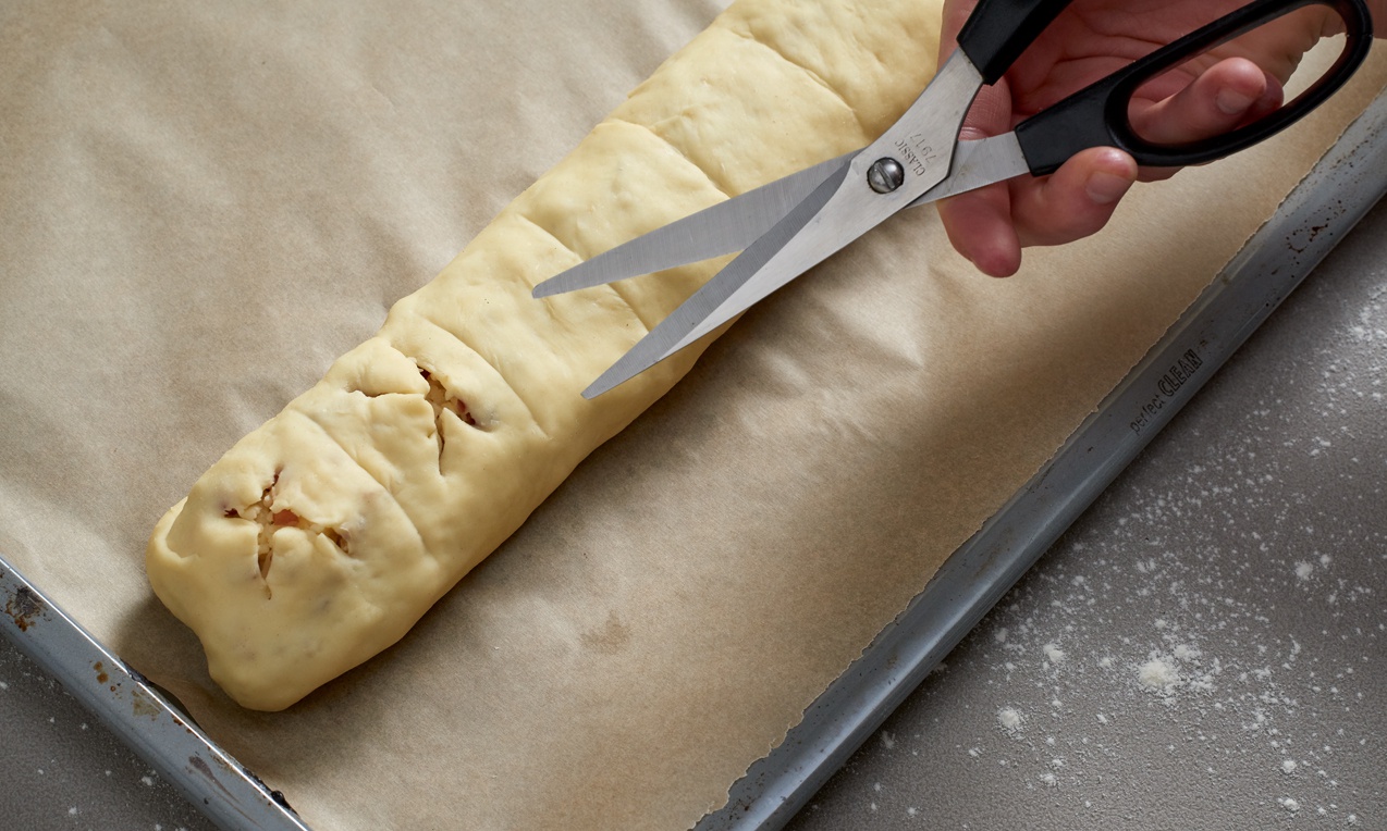 A feltekert Töltött házi bagett tetejét megkenjük, majd ollóval cakkokat vágunk bele.