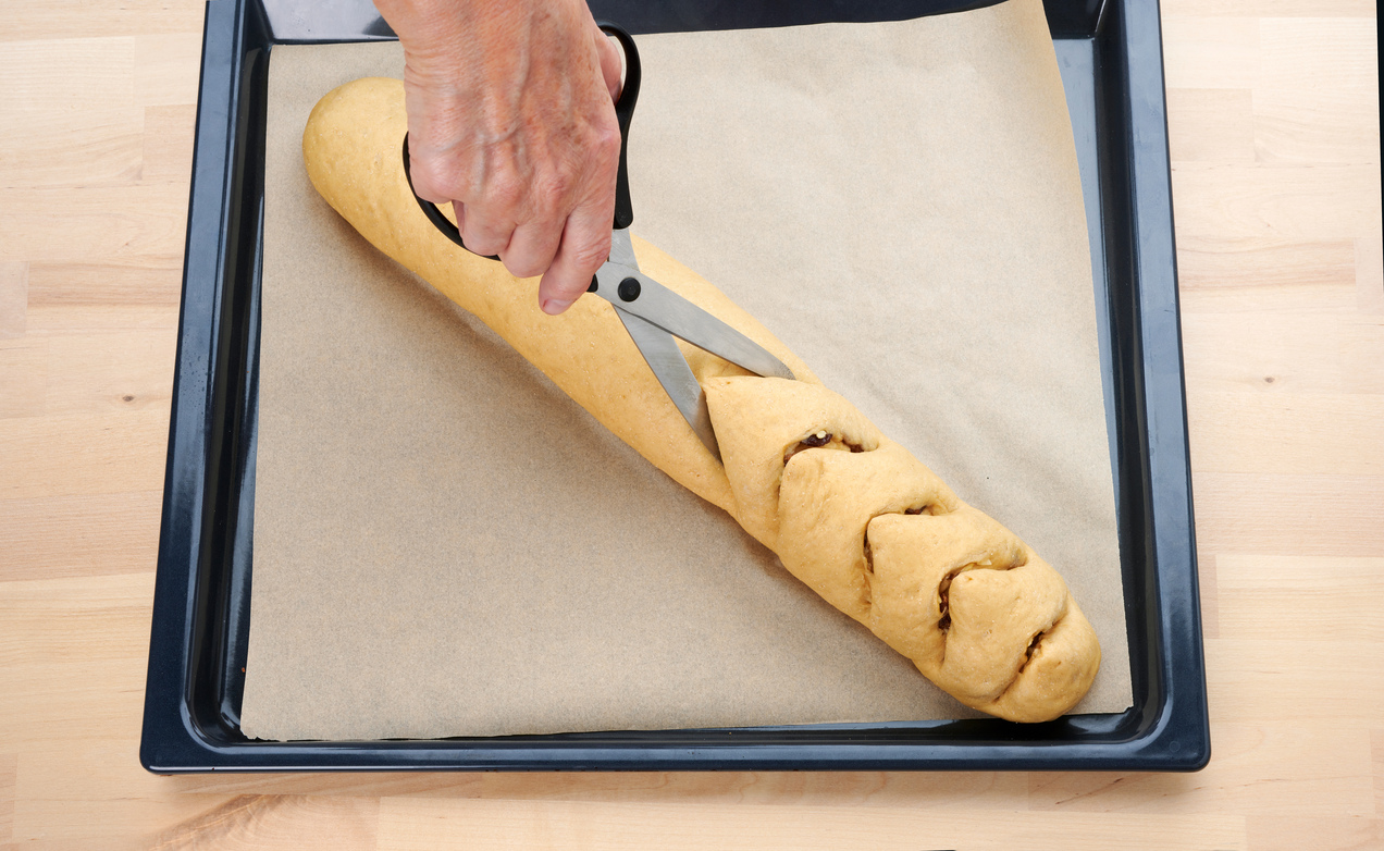 A megtöltött és feltekert Marcipános-mazsolás copf süteményt konyhai ollóval bevagdossuk.